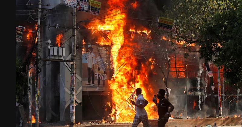 Dos hombres corren frente a un centro comercial incendiado durante las protestas de este domingo contra la primera ministra Sheikh Hasima. Rajib Dhar (AP)