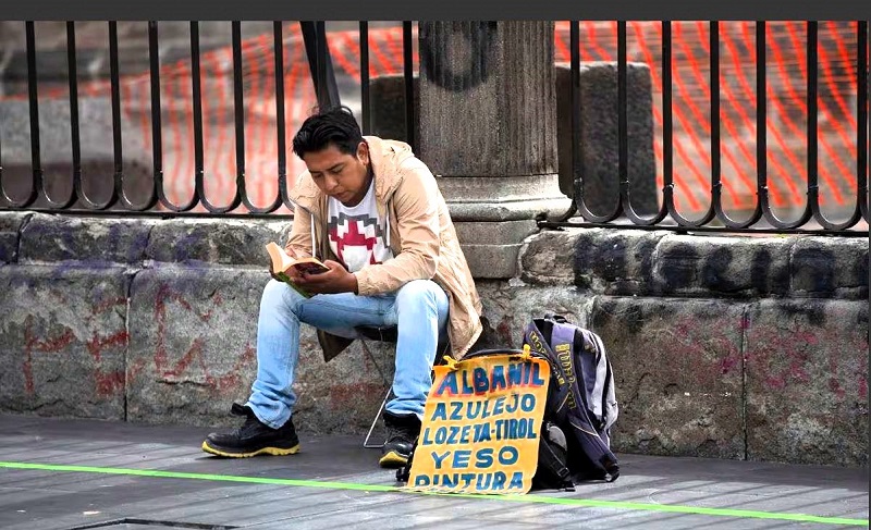 Un hombre lee mientras ofrece servicios de albañilería, frente a la Catedral Metropolitana en Ciudad de México, en agosto de 2020. MARCO UGARTE (AP)