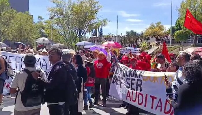 Dos personas cargan una pancarta blanca que dice "El maestro luchando también están enseñando" en un parque. La protesta en la BUAP. (Especial)