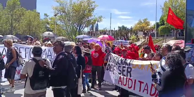 Dos personas cargan una pancarta blanca que dice "El maestro luchando también están enseñando" en un parque. La protesta en la BUAP. (Especial)